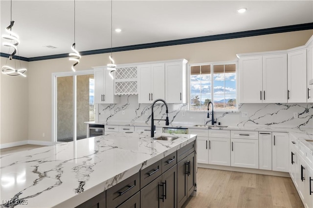 kitchen featuring sink, white cabinets, hanging light fixtures, ornamental molding, and light stone counters