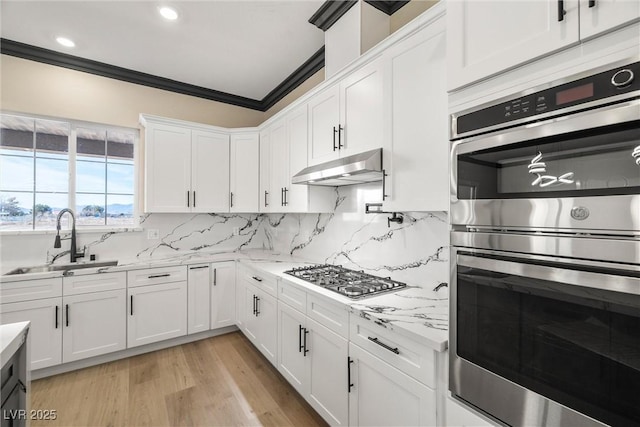 kitchen with sink, appliances with stainless steel finishes, white cabinetry, ornamental molding, and light stone countertops