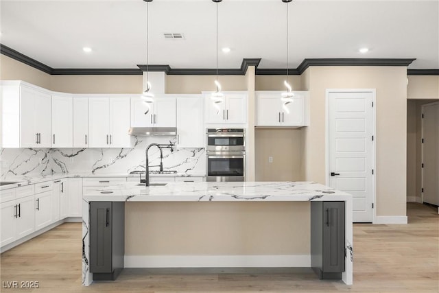 kitchen featuring pendant lighting, white cabinets, a kitchen island with sink, light stone counters, and stainless steel double oven