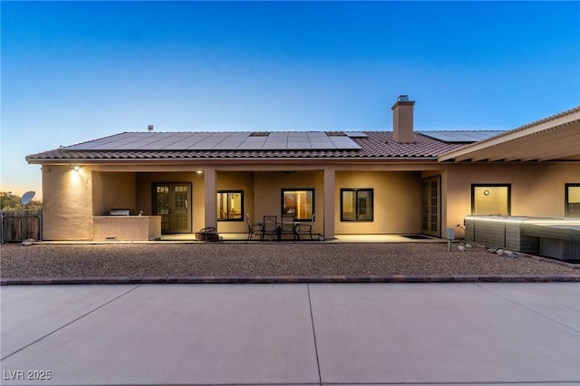 back house at dusk with a patio and solar panels