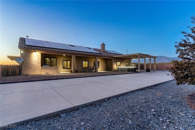 back house at dusk featuring a jacuzzi, a pergola, a patio, and solar panels