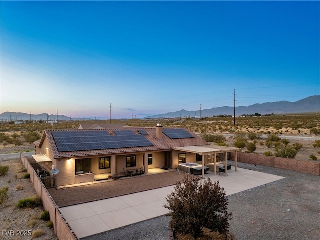 back house at dusk featuring a patio, a mountain view, and solar panels