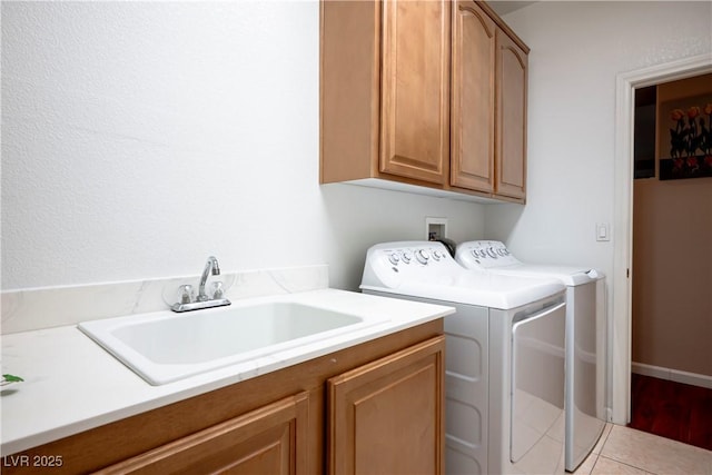 clothes washing area with sink, light tile patterned floors, washing machine and dryer, and cabinets