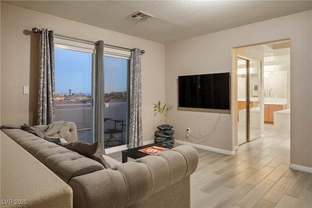 living room featuring light wood-style floors, visible vents, and baseboards