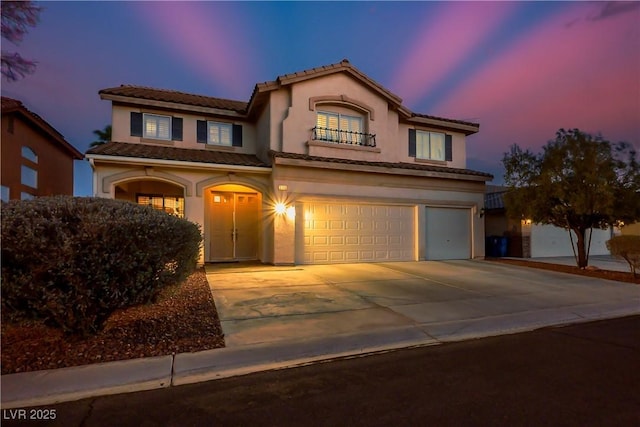 mediterranean / spanish-style home with driveway, a tiled roof, an attached garage, and stucco siding