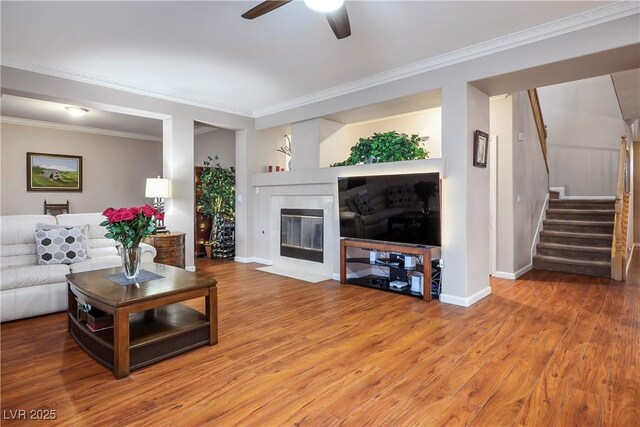 living room with crown molding, ceiling fan, wood-type flooring, and a fireplace