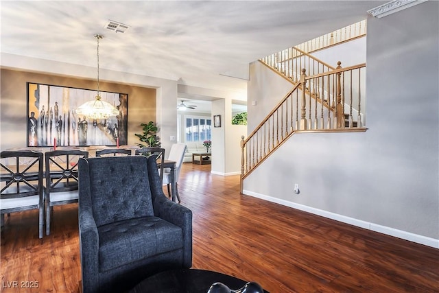 living room with visible vents, stairway, wood finished floors, baseboards, and ceiling fan with notable chandelier