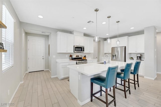 kitchen featuring appliances with stainless steel finishes, white cabinetry, sink, hanging light fixtures, and a kitchen island with sink