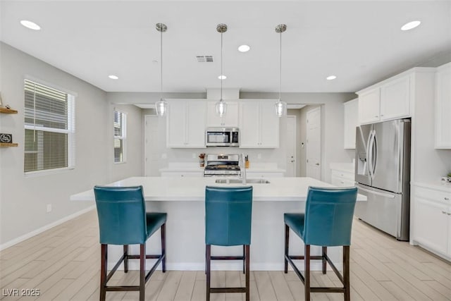 kitchen with pendant lighting, stainless steel appliances, and a center island with sink