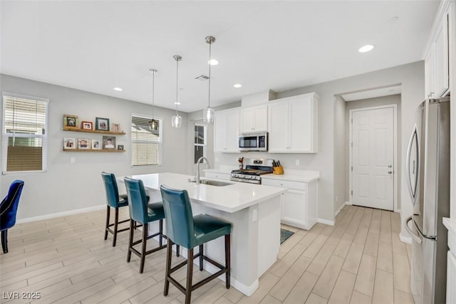 kitchen featuring sink, appliances with stainless steel finishes, white cabinetry, hanging light fixtures, and an island with sink