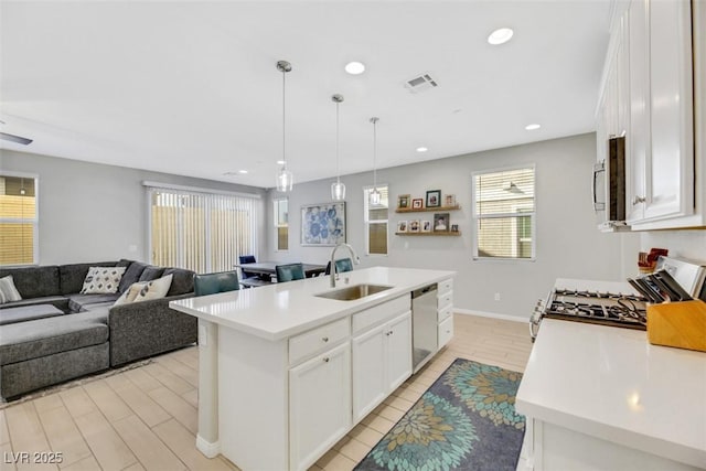 kitchen with sink, white cabinetry, stainless steel appliances, an island with sink, and decorative light fixtures