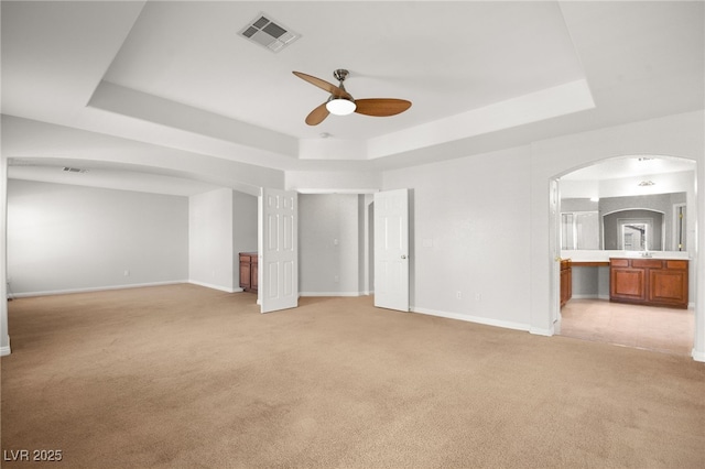 unfurnished bedroom featuring light carpet, a tray ceiling, ceiling fan, and ensuite bathroom