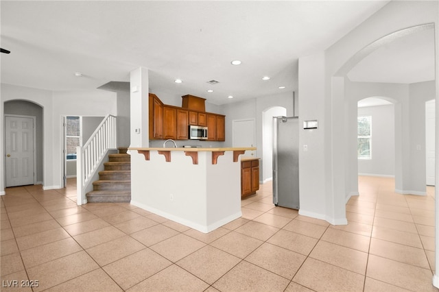 kitchen featuring light tile patterned floors, a breakfast bar area, stainless steel appliances, and kitchen peninsula