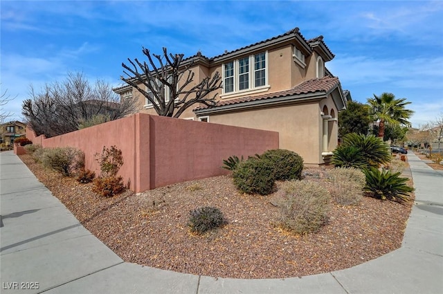 view of side of home featuring a tile roof, fence, and stucco siding