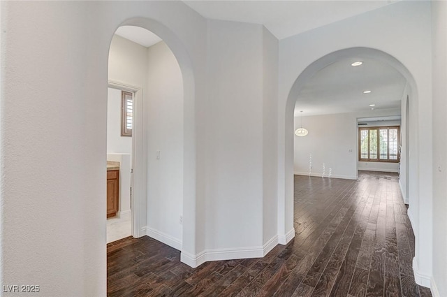 hall featuring dark wood-type flooring, arched walkways, and baseboards