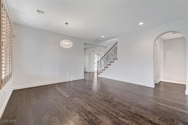 spare room with arched walkways, dark wood-style floors, visible vents, and baseboards