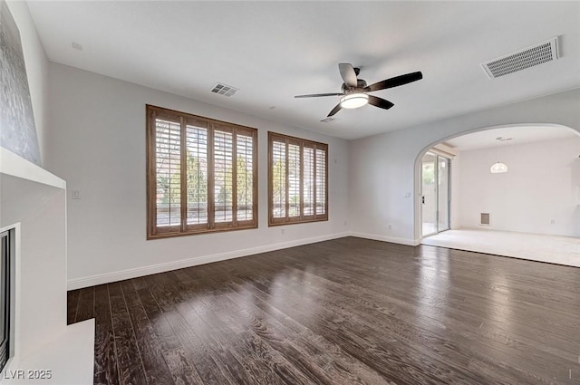 unfurnished living room with arched walkways, dark wood-type flooring, visible vents, and a ceiling fan