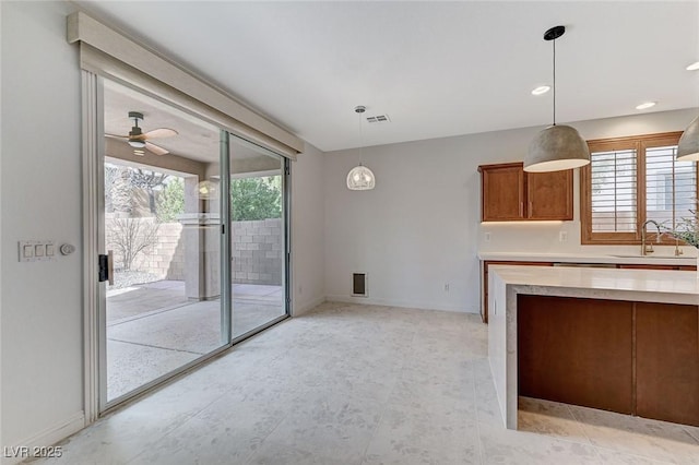 kitchen with visible vents, brown cabinets, light countertops, pendant lighting, and a sink