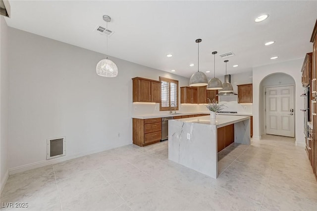 kitchen with visible vents, arched walkways, wall chimney exhaust hood, brown cabinets, and a center island