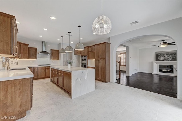 kitchen featuring arched walkways, open floor plan, a sink, stovetop, and wall chimney exhaust hood