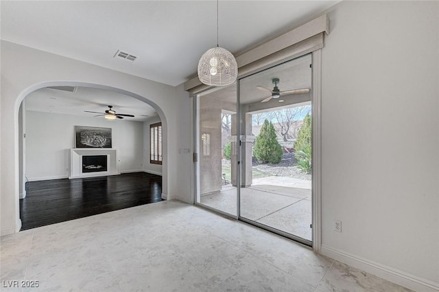 unfurnished living room with arched walkways, a fireplace, visible vents, a ceiling fan, and baseboards