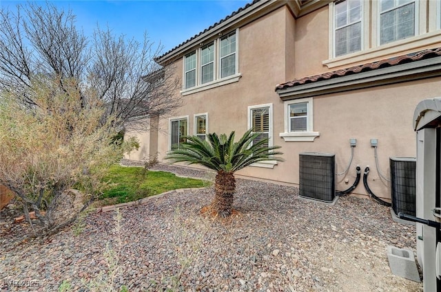 view of property exterior featuring a tiled roof, cooling unit, and stucco siding