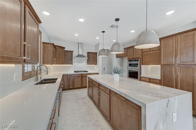 kitchen featuring wall chimney range hood, sink, stainless steel appliances, a spacious island, and decorative light fixtures