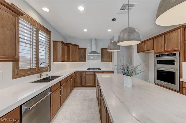 kitchen featuring appliances with stainless steel finishes, decorative light fixtures, sink, light stone countertops, and wall chimney range hood