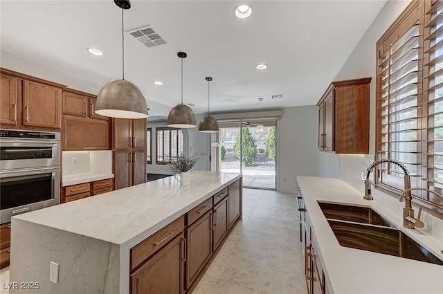 kitchen with pendant lighting, sink, double oven, light stone counters, and a kitchen island