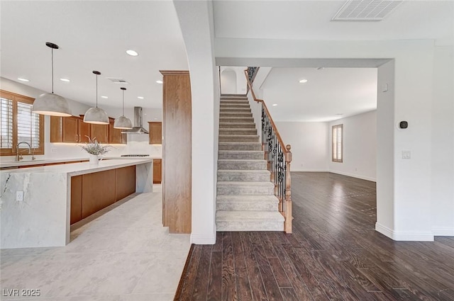 kitchen featuring visible vents, wall chimney exhaust hood, brown cabinets, light countertops, and light wood-style floors