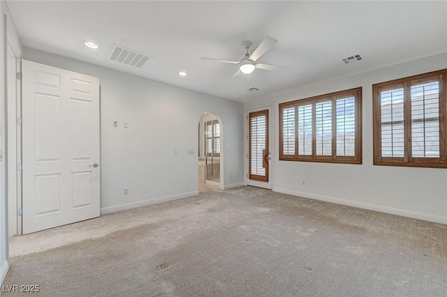 empty room featuring visible vents, arched walkways, and light colored carpet