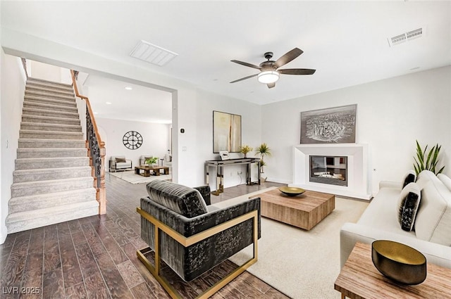 living area featuring wood finished floors, visible vents, a ceiling fan, stairway, and a glass covered fireplace