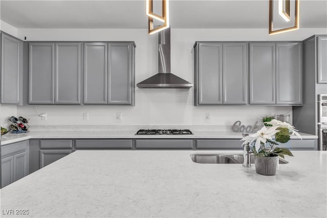 kitchen featuring light stone counters, wall chimney exhaust hood, stainless steel gas stovetop, and gray cabinetry