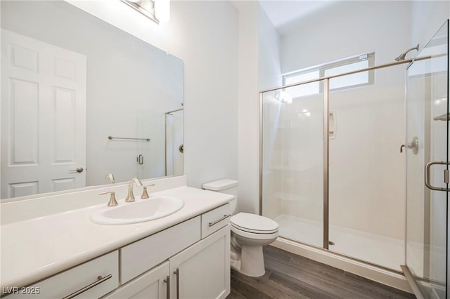 full bath featuring toilet, wood finished floors, vanity, and a shower stall