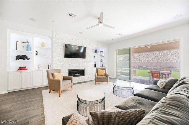 living area featuring ceiling fan, a fireplace, wood finished floors, visible vents, and built in features