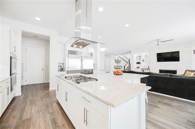 kitchen featuring light stone counters, light wood-style flooring, white cabinets, appliances with stainless steel finishes, and a center island