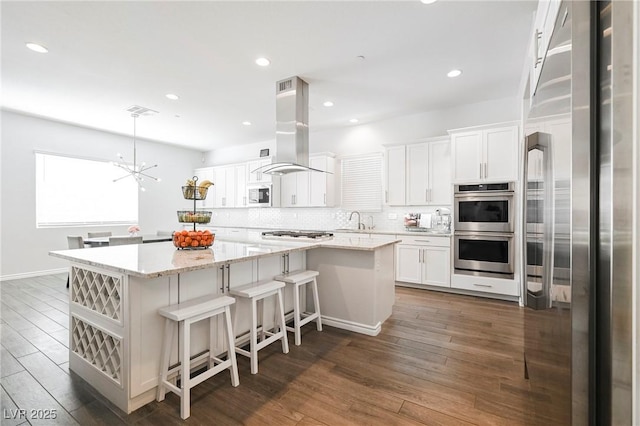 kitchen with a center island, appliances with stainless steel finishes, white cabinets, island range hood, and light stone countertops