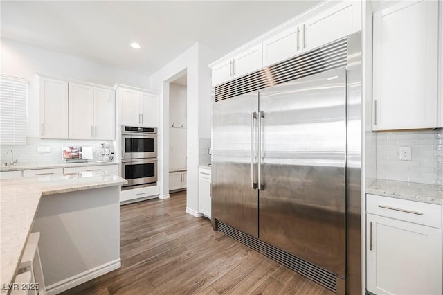 kitchen with light stone counters, stainless steel appliances, tasteful backsplash, white cabinetry, and wood finished floors