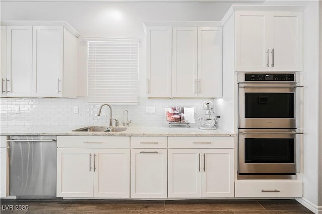 kitchen with light stone counters, stainless steel appliances, dark wood-type flooring, white cabinetry, and a sink