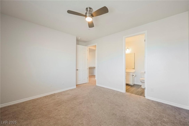 unfurnished bedroom featuring light colored carpet, a ceiling fan, baseboards, a walk in closet, and ensuite bath