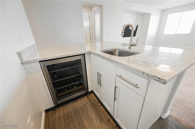 kitchen featuring beverage cooler, dark wood-type flooring, light stone countertops, white cabinetry, and a sink