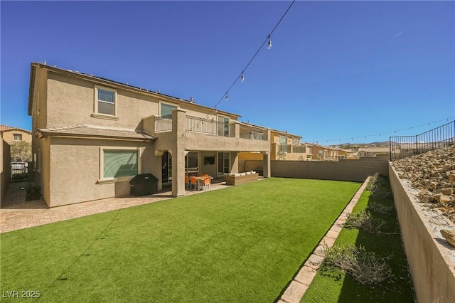 back of property featuring a fenced backyard, a balcony, a yard, stucco siding, and a patio area