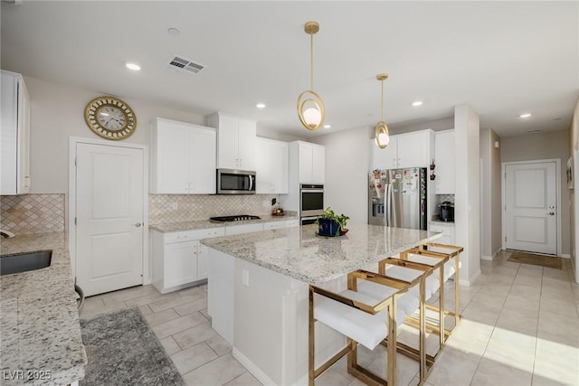 kitchen featuring white cabinetry, appliances with stainless steel finishes, decorative light fixtures, and light stone countertops