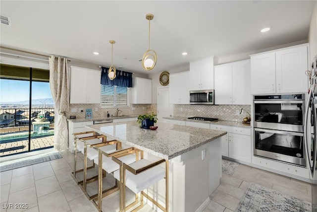 kitchen with appliances with stainless steel finishes, a center island, pendant lighting, and white cabinets