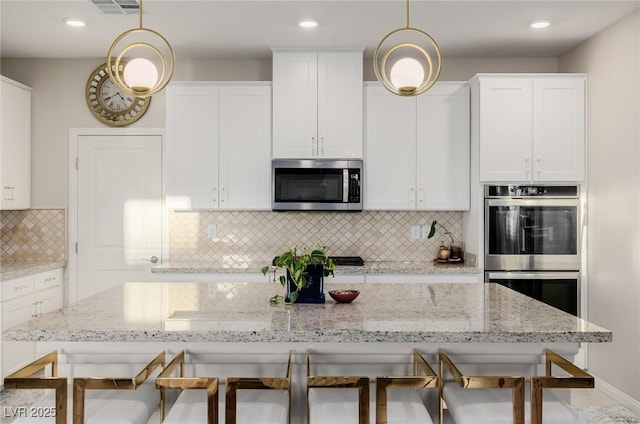 kitchen featuring stainless steel appliances, white cabinetry, pendant lighting, and a kitchen breakfast bar