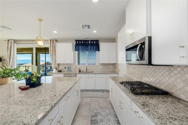 kitchen with white cabinetry, hanging light fixtures, backsplash, stainless steel appliances, and light stone counters