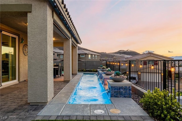 pool at dusk with a patio area and pool water feature