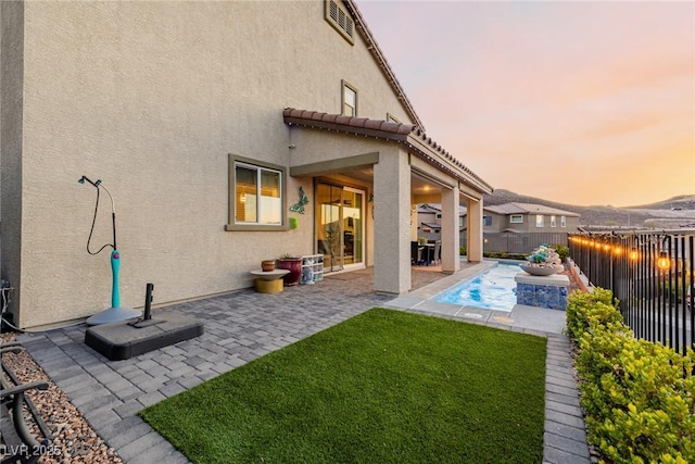 back house at dusk with a fenced in pool, a yard, and a patio area