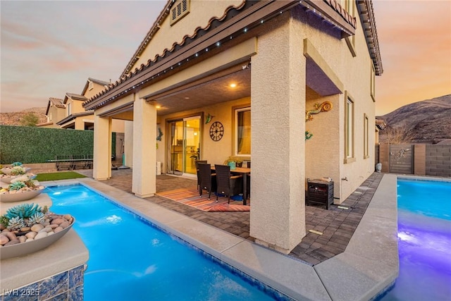 pool at dusk with pool water feature and a patio area