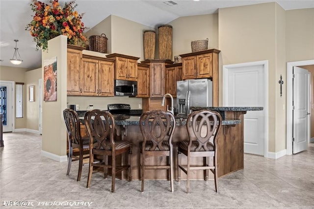 kitchen featuring appliances with stainless steel finishes, a kitchen island with sink, high vaulted ceiling, and a kitchen bar